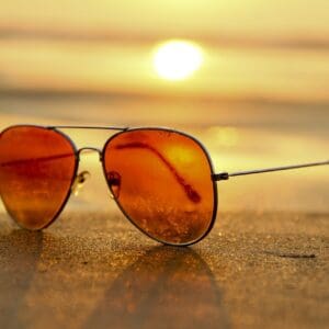 A pair of sunglasses on the sand at sunset.