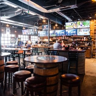 The inside of a bar with stools and televisions.